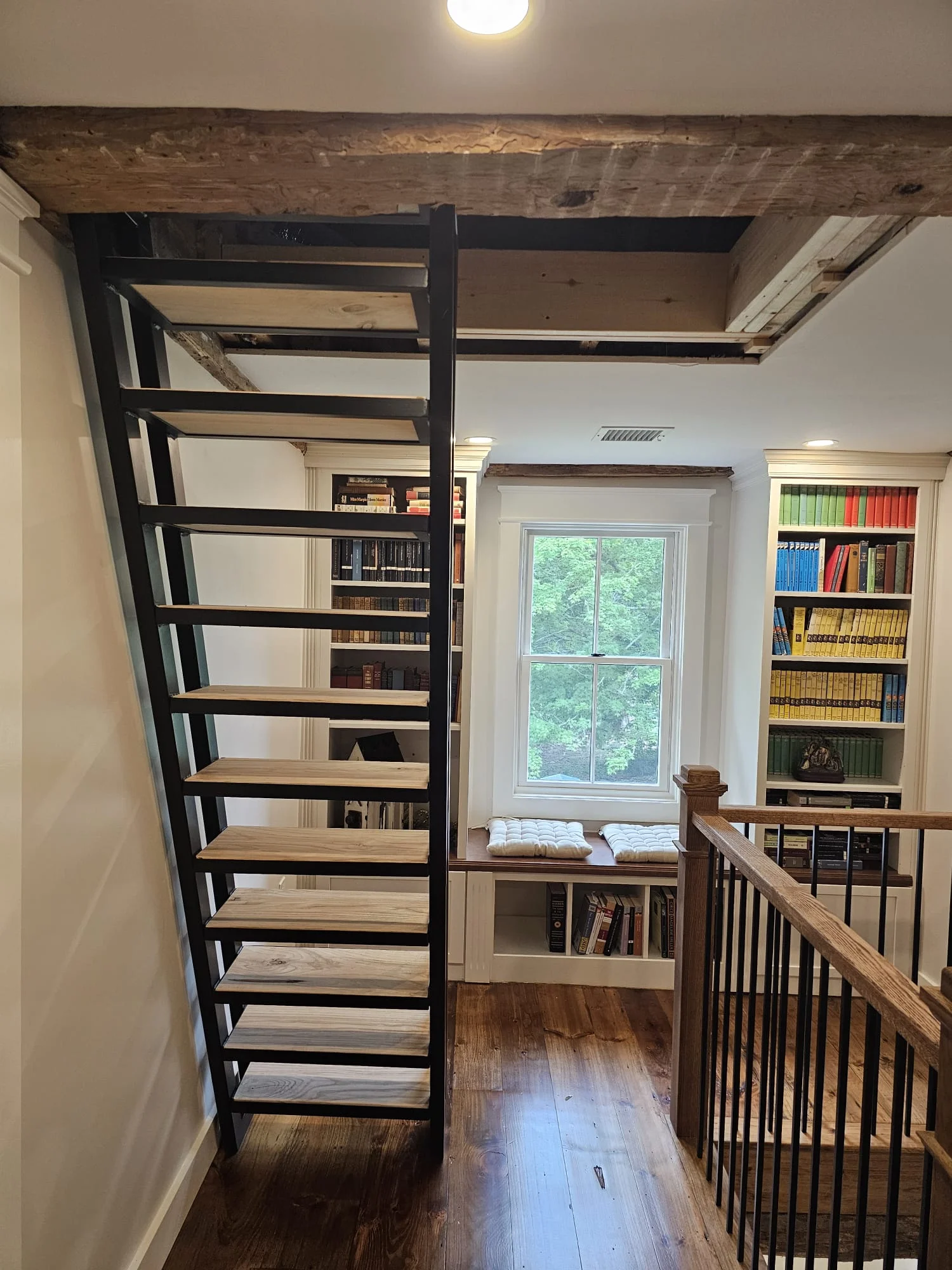 Black metal staircase with wood treads leading to loft, flanked by built-in bookshelves