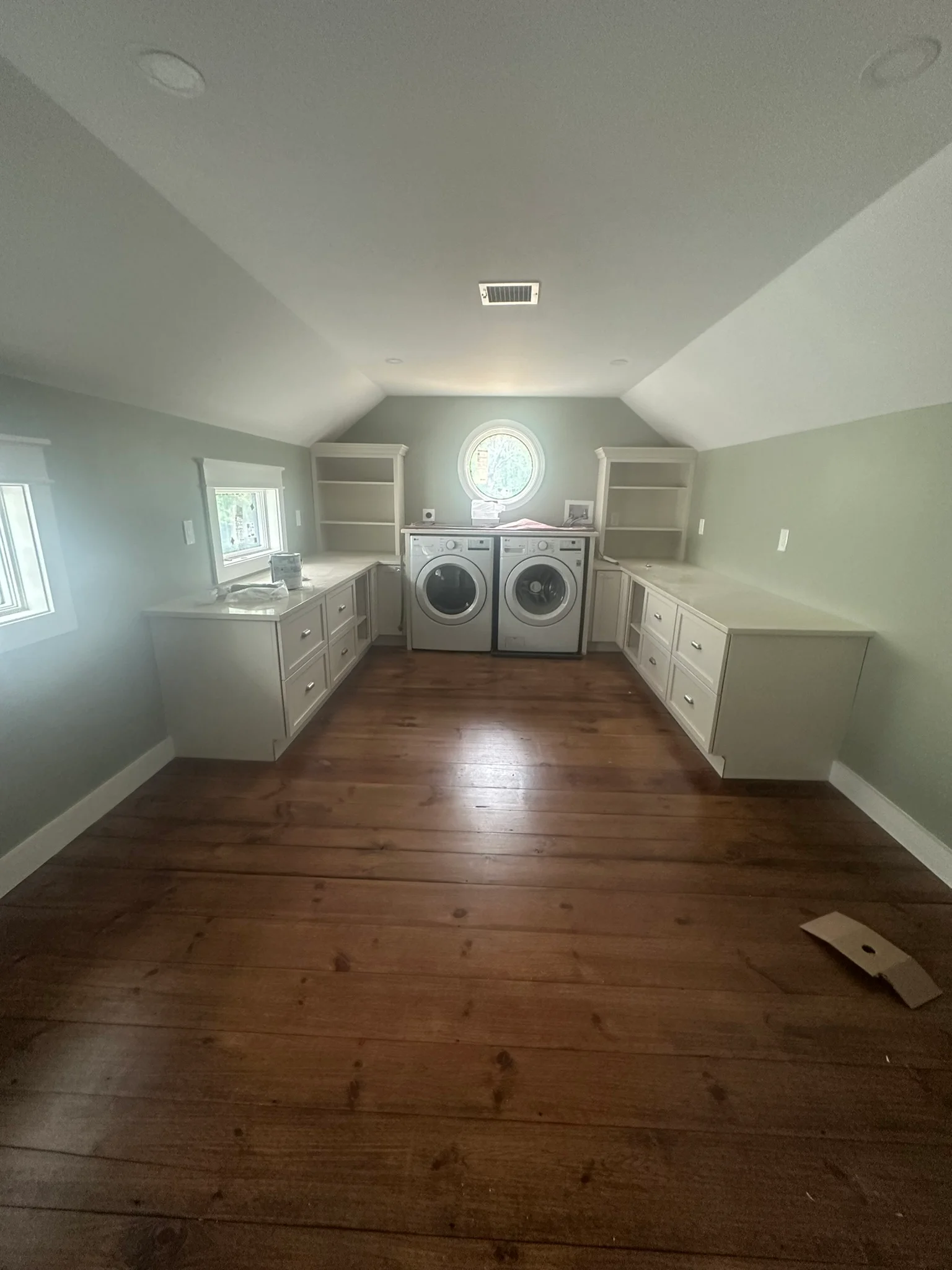 Bright laundry room with white cabinetry, dual washers/dryers, hardwood floors, and vaulted ceiling