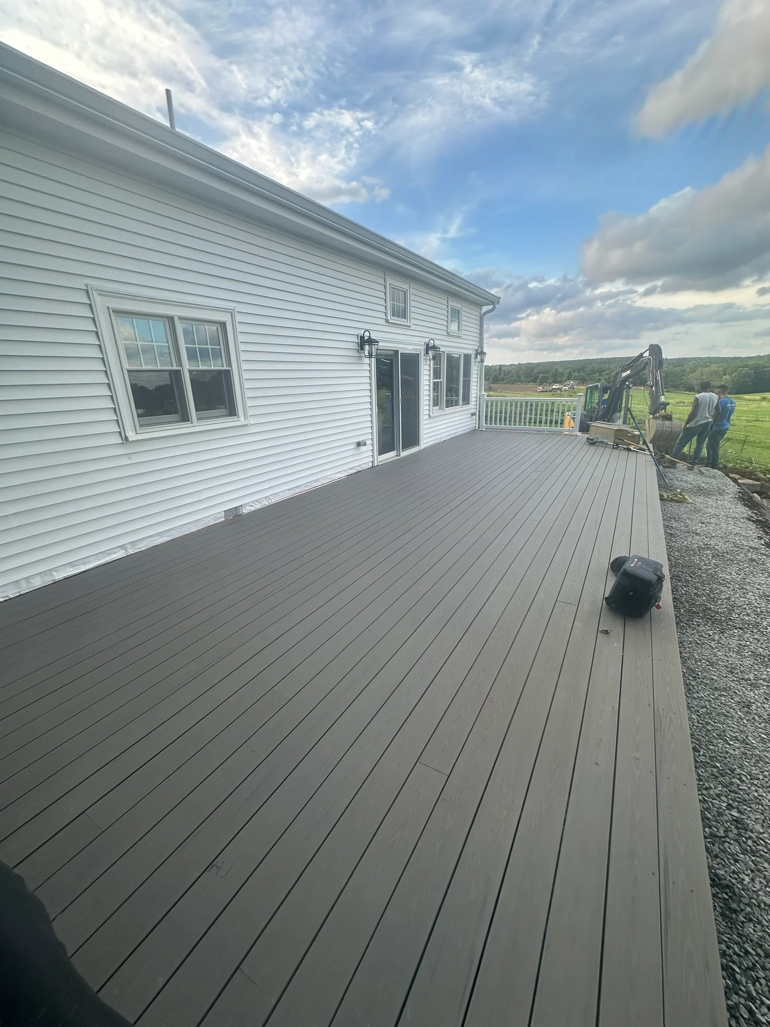 Gray composite deck with white house, glass doors, and rural landscape views — General Contractor work by Innovative Build Solutions.