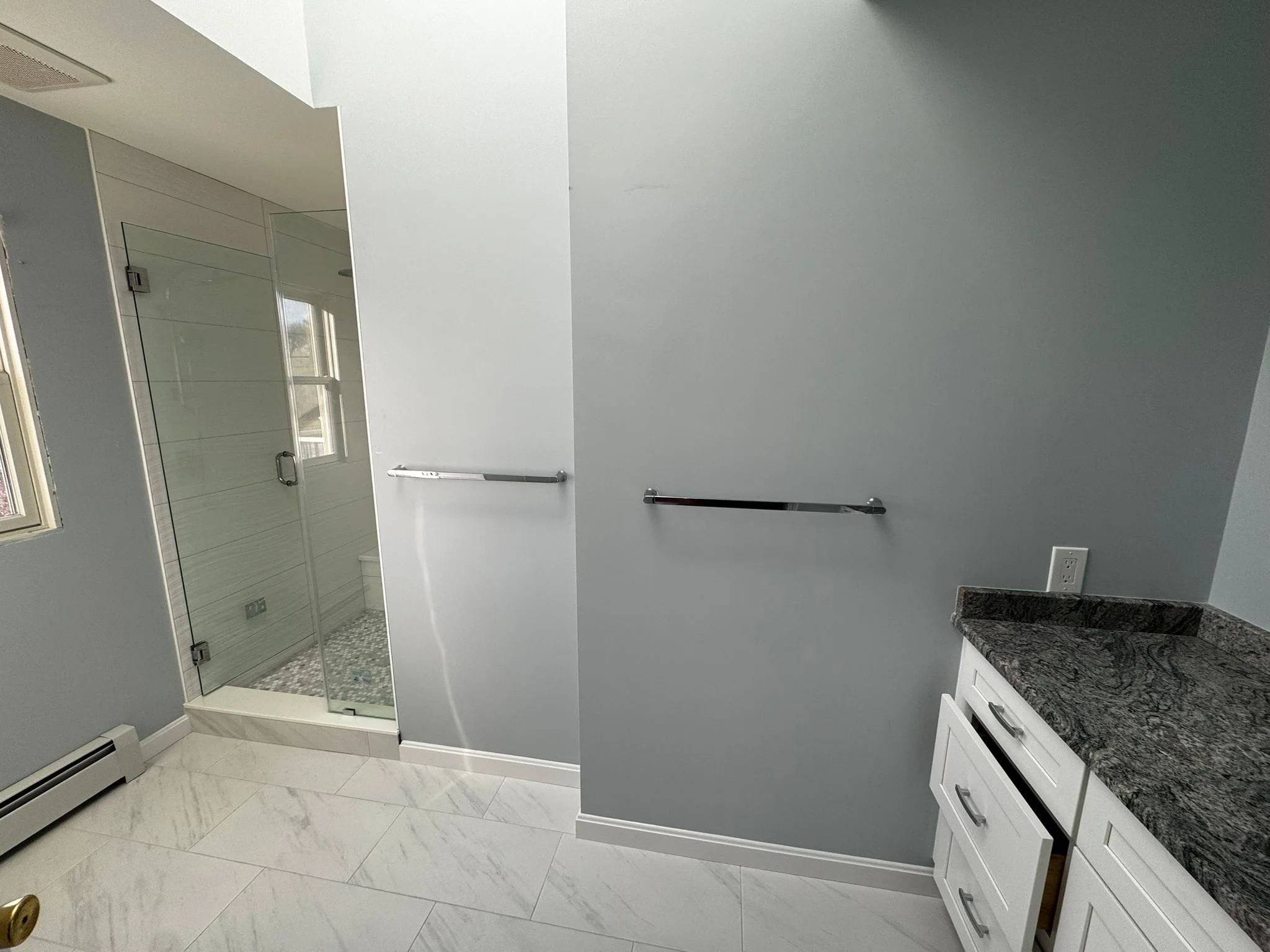 Modern bathroom with frameless shower, marble floors, white vanity, and gray walls