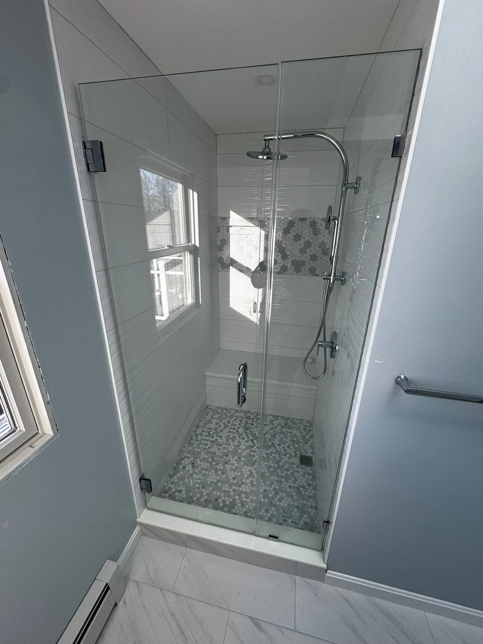 Modern frameless glass shower with white subway tile and mosaic floor in Sterling bathroom