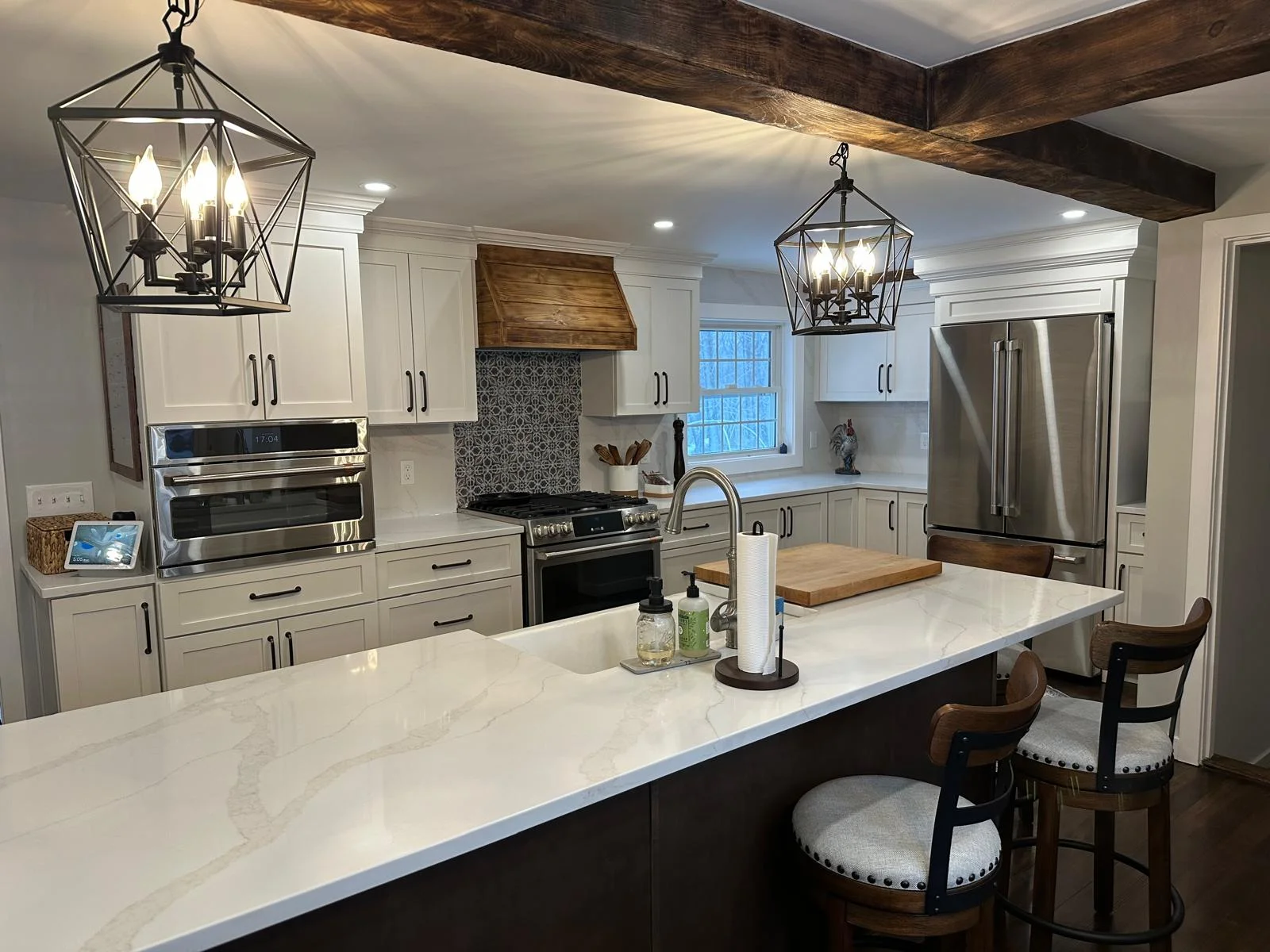Modern kitchen with white cabinets, marble countertops, dark island, and pendant lighting — Kitchen Remodeling by Innovative Build Solutions.
