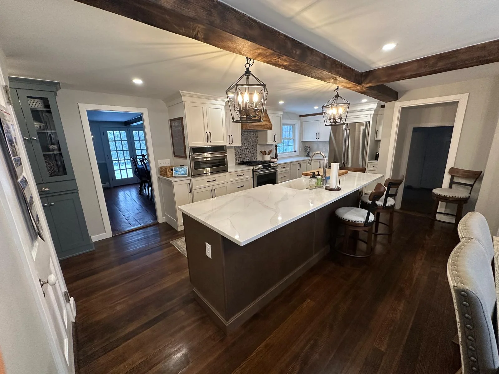 Modern kitchen with white cabinets, dark island, quartz countertops, and exposed wood beams — Full-Home Remodeling by Innovative Build Solutions.
